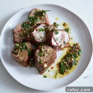 Grilled Pork Tenderloin with Fresh Chimichurri Sauce 9 Slices of grilled pork tenderloin with chimichurri sauce on a white plate.