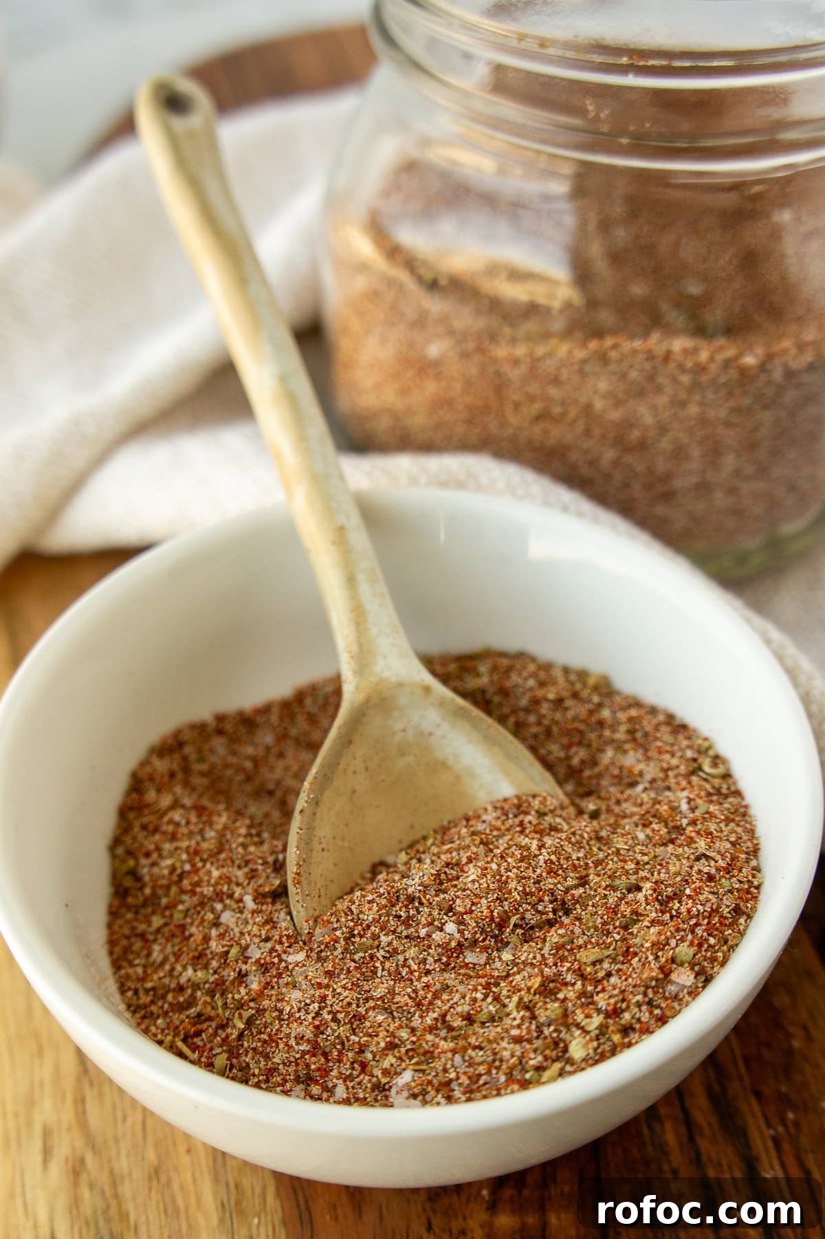 a white bowl of mixed spices with a white spoon and mason jar.