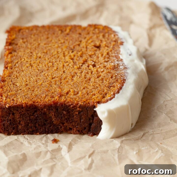 a slice of gluten free pumpkin bread topped with cream cheese frosting on brown parchment paper