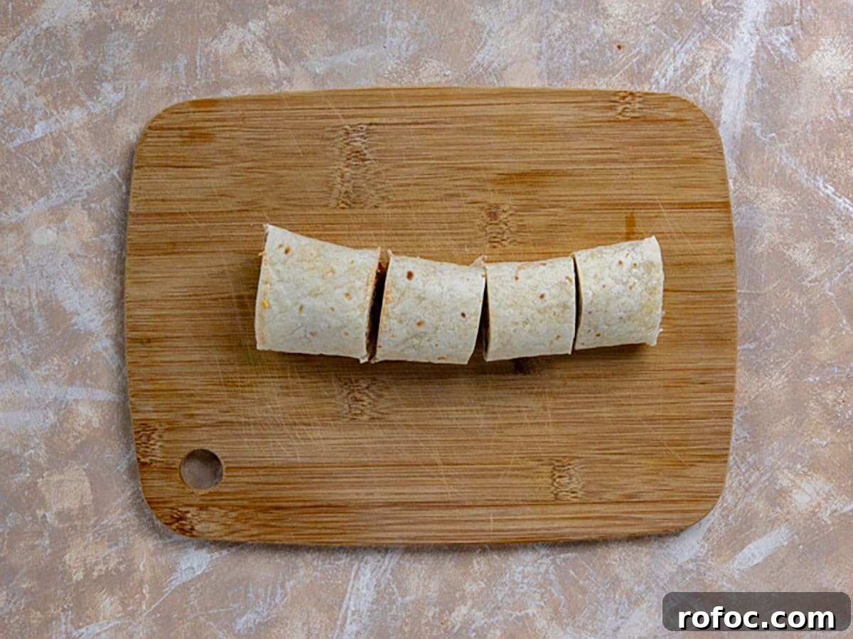 Taco Meat Pinwheels: Quick Party Appetizers from Leftovers 6 One complete pinwheel sliced into 4 pieces on a wooden cutting board.