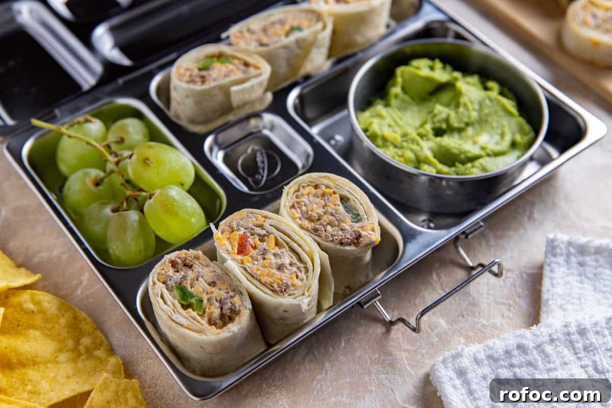 Taco Meat Pinwheels: Quick Party Appetizers from Leftovers 7 Taco meat pinwheels in a stainless steel meal prep container with guacamole and green grapes on the side.