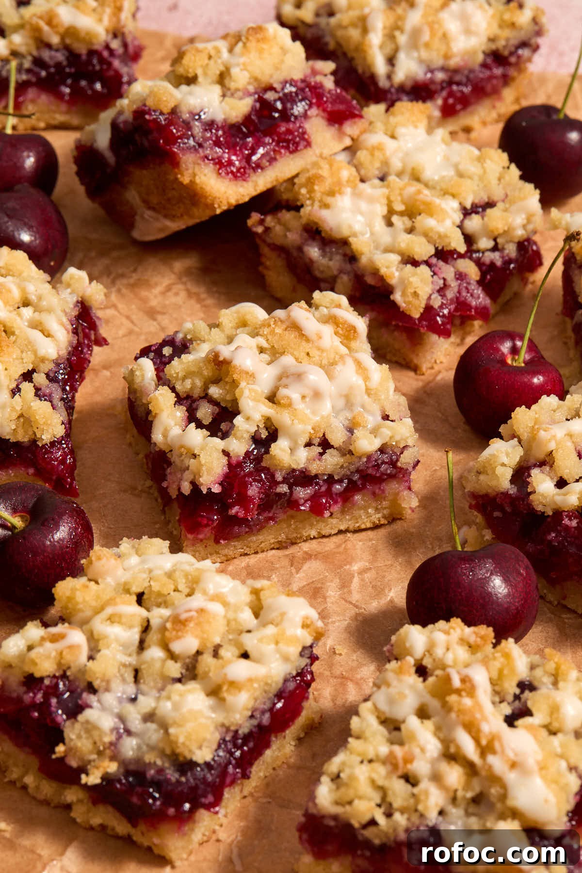 Almond Flour Cherry Pie Bars Recipe — Tender Cherry Dessert Bars 15 Cherry pie bars arranged on parchment with cherries around them.