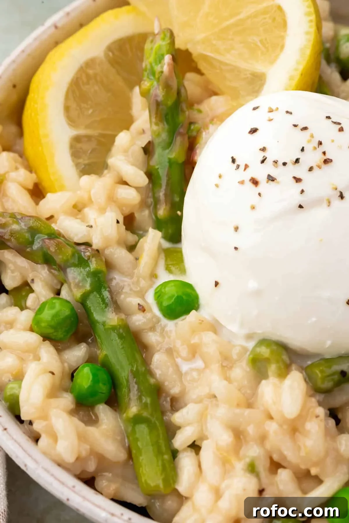 Creamy Asparagus and Pea Risotto with Burrata Cheese 12 A closeup of a bowl of risotto with peas and asparagus topped with a ball of burrata sprinkled with black pepper and a lemon wedge.