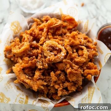fried onions in wooden bowl with salt and bbq sauce blurred in background