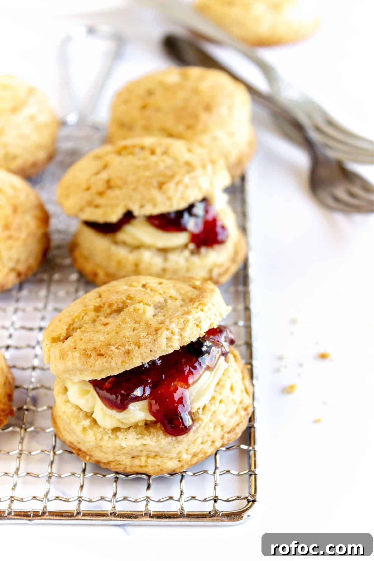 Mini Cream Scones Recipe — Simple Homemade Bite-Sized Scones 11 Wire rack with scones filled with jam. White surface.