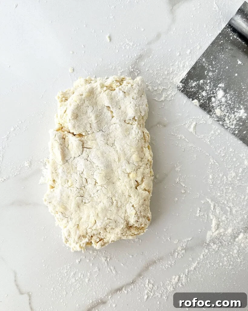 Mini Cream Scones Recipe — Simple Homemade Bite-Sized Scones 8 Folded shabby biscuit dough on white marble. Metal scraper.