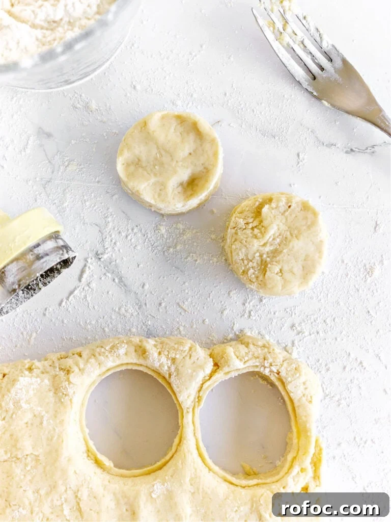 Mini Cream Scones Recipe — Simple Homemade Bite-Sized Scones 9 Scone dough on a white surface, cookie cutter, cut scones, silver fork.