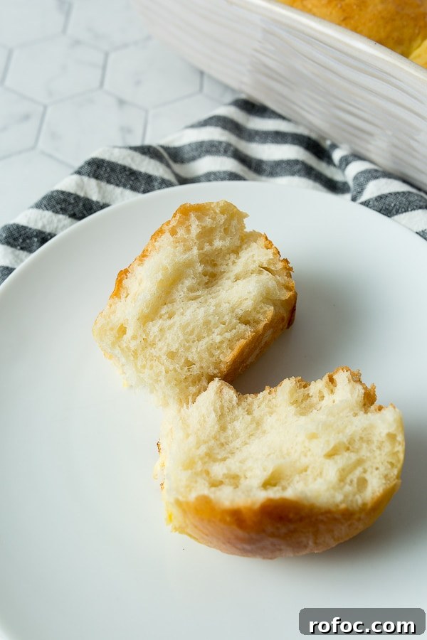 Soft Homemade Dinner Rolls Recipe: Fluffy Yeast Rolls for Any Meal 4 one bread roll split in half on a small white plate with a blue and towel on the side.