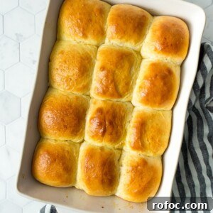 Soft Homemade Dinner Rolls Recipe: Fluffy Yeast Rolls for Any Meal 5 a dozen baked dinner rolls in a white baking dish on top of a white and blue kitchen towel.