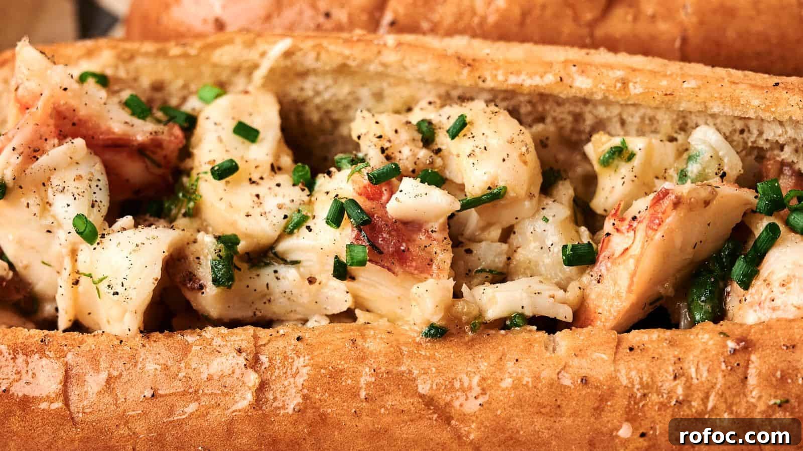 35 Gameday Recipes That Always Crowd-Pleasers Love 19 A close-up of a sandwich roll filled with chunks of seasoned lobster meat, garnished with chopped chives.