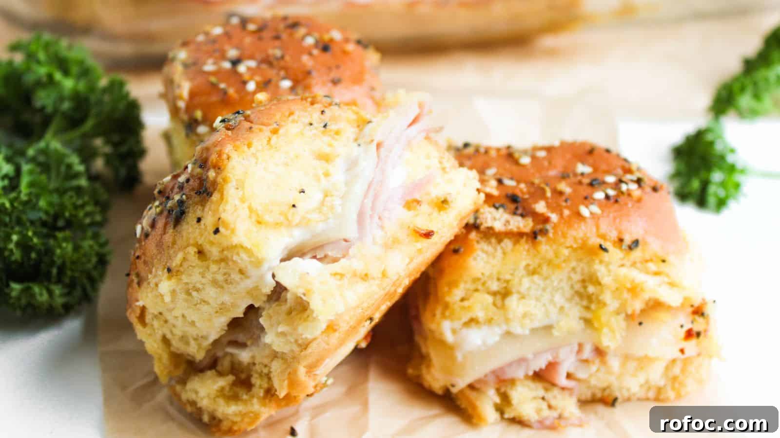 35 Gameday Recipes That Always Crowd-Pleasers Love 21 Three ham and cheese sliders on seeded buns are placed on parchment paper. Bright green parsley is visible in the background.