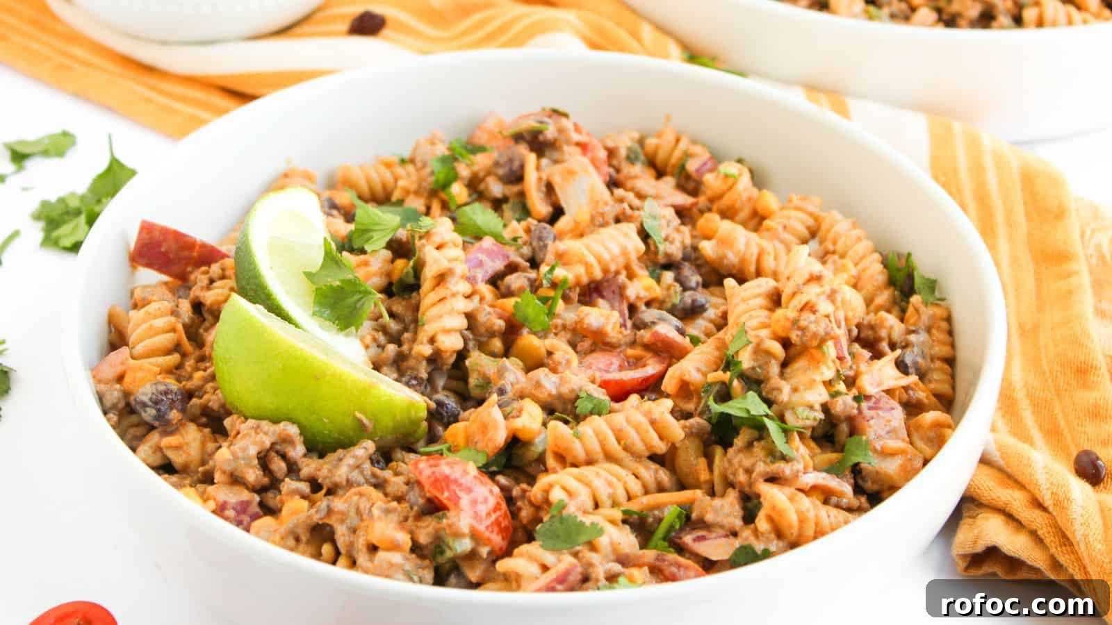 35 Gameday Recipes That Always Crowd-Pleasers Love 27 A bowl of fusilli pasta mixed with ground beef, black beans, chopped tomatoes, and herbs, garnished with lime wedges.