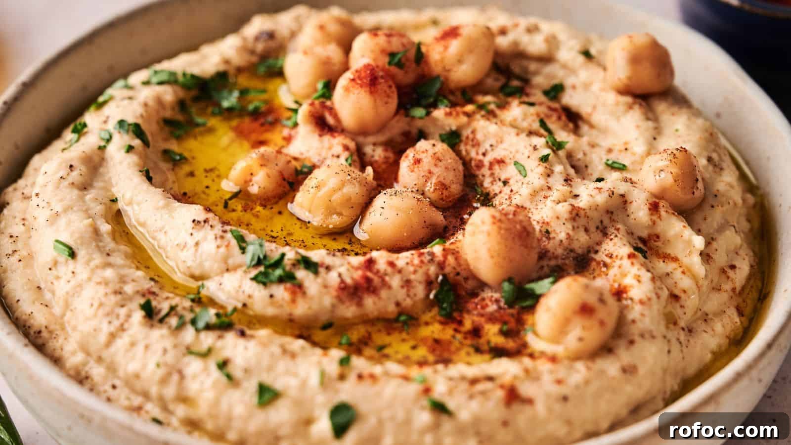 35 Gameday Recipes That Always Crowd-Pleasers Love 4 A bowl of hummus garnished with whole chickpeas, chopped parsley, paprika, and a drizzle of olive oil.