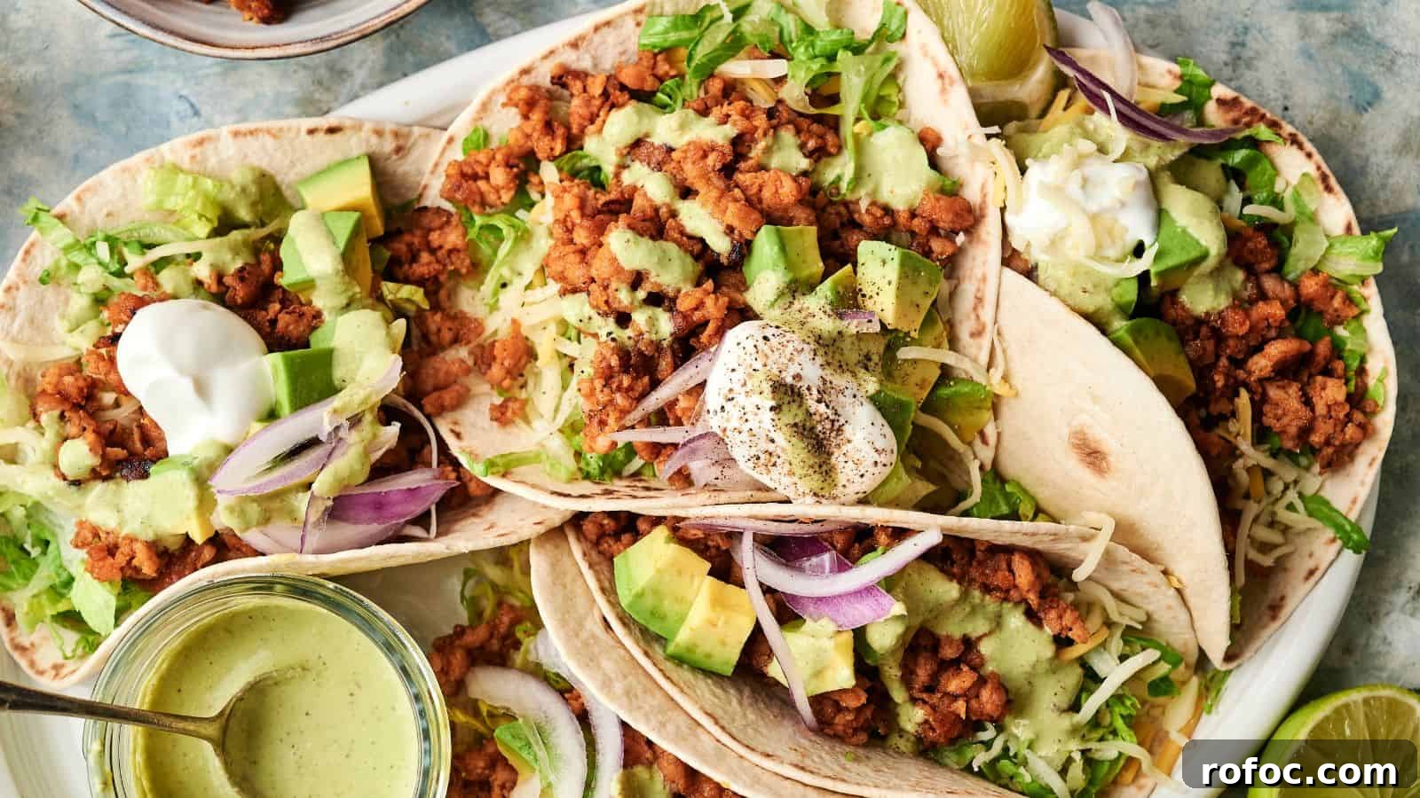 35 Gameday Recipes That Always Crowd-Pleasers Love 33 Three soft tacos filled with seasoned ground meat, shredded lettuce, diced avocado, red onion, shredded cheese, and topped with sour cream and green sauce sit on a plate.