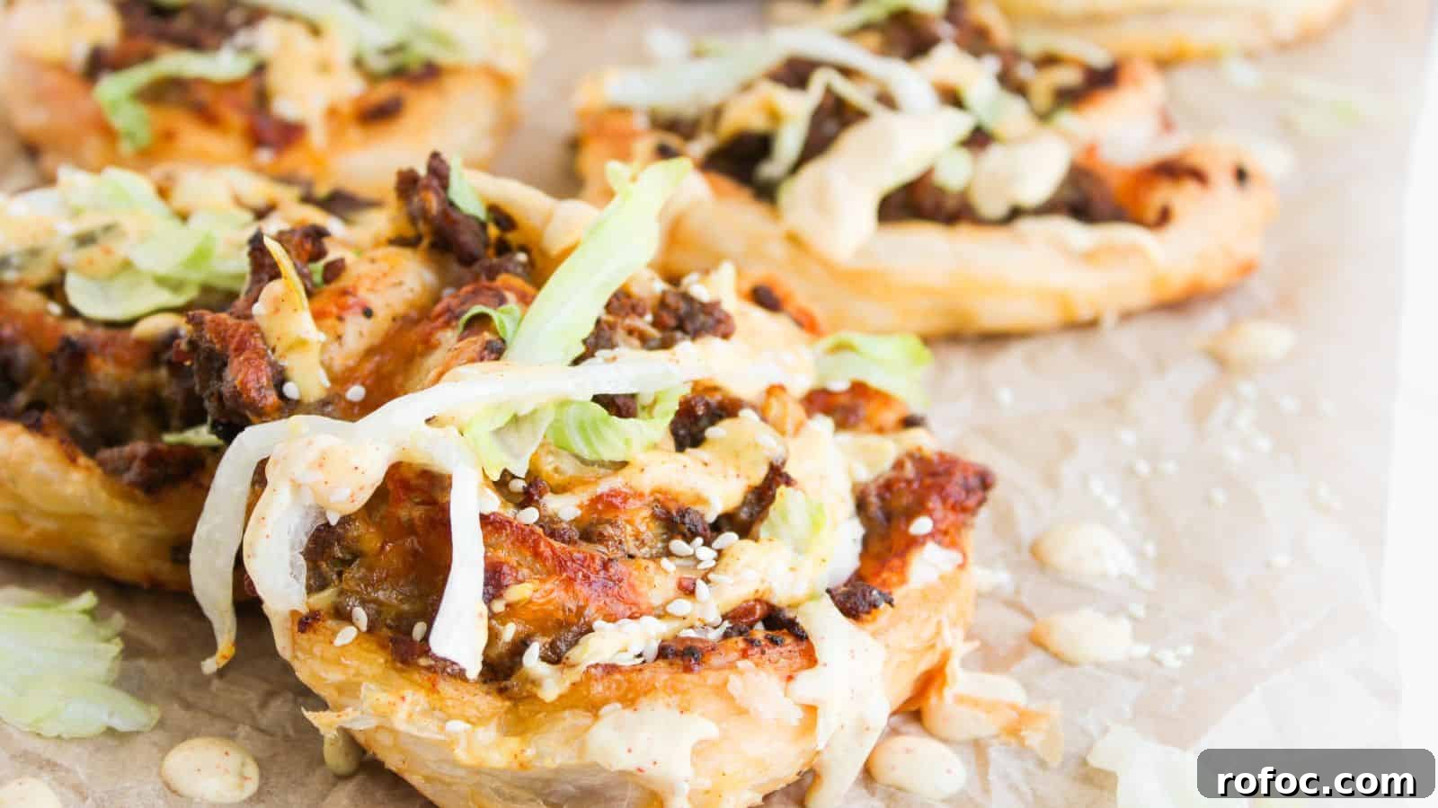 35 Gameday Recipes That Always Crowd-Pleasers Love 5 Close-up of puff pastry rounds topped with ground meat, shredded lettuce, sesame seeds, and a creamy sauce, arranged on parchment paper.