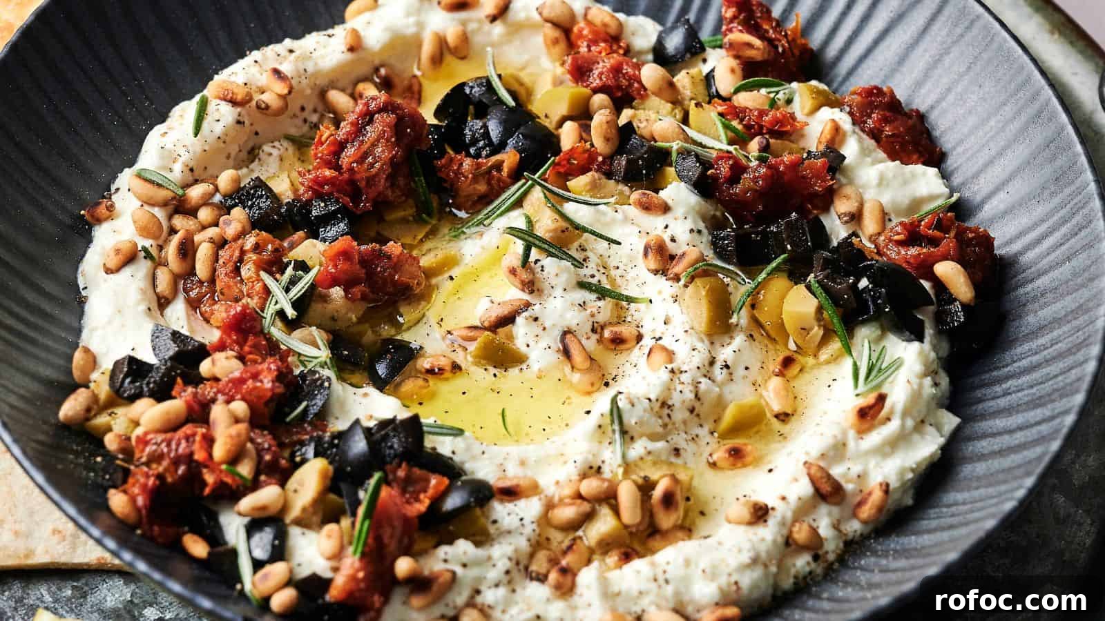 35 Gameday Recipes That Always Crowd-Pleasers Love 9 A bowl of creamy dip garnished with chopped black olives, sun-dried tomatoes, pine nuts, rosemary, olive oil, and black pepper.