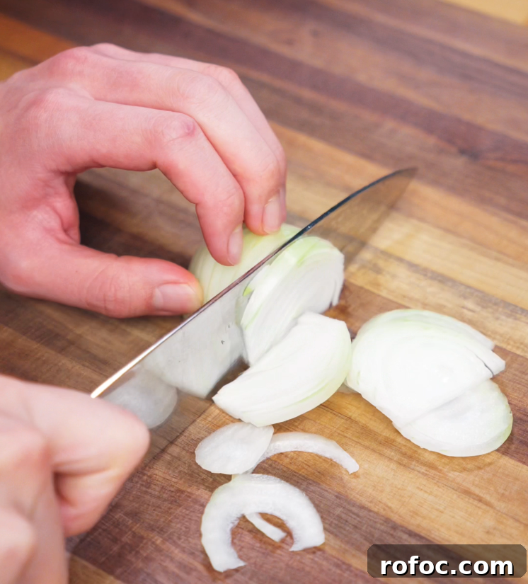 Savory Beef Curry Udon Recipe for Comforting Weeknight Meals 4 A hand holds a knife while slicing a white onion into thin half-moons on a wooden cutting board. These onions will add sweetness and depth to the savory Japanese curry broth.
