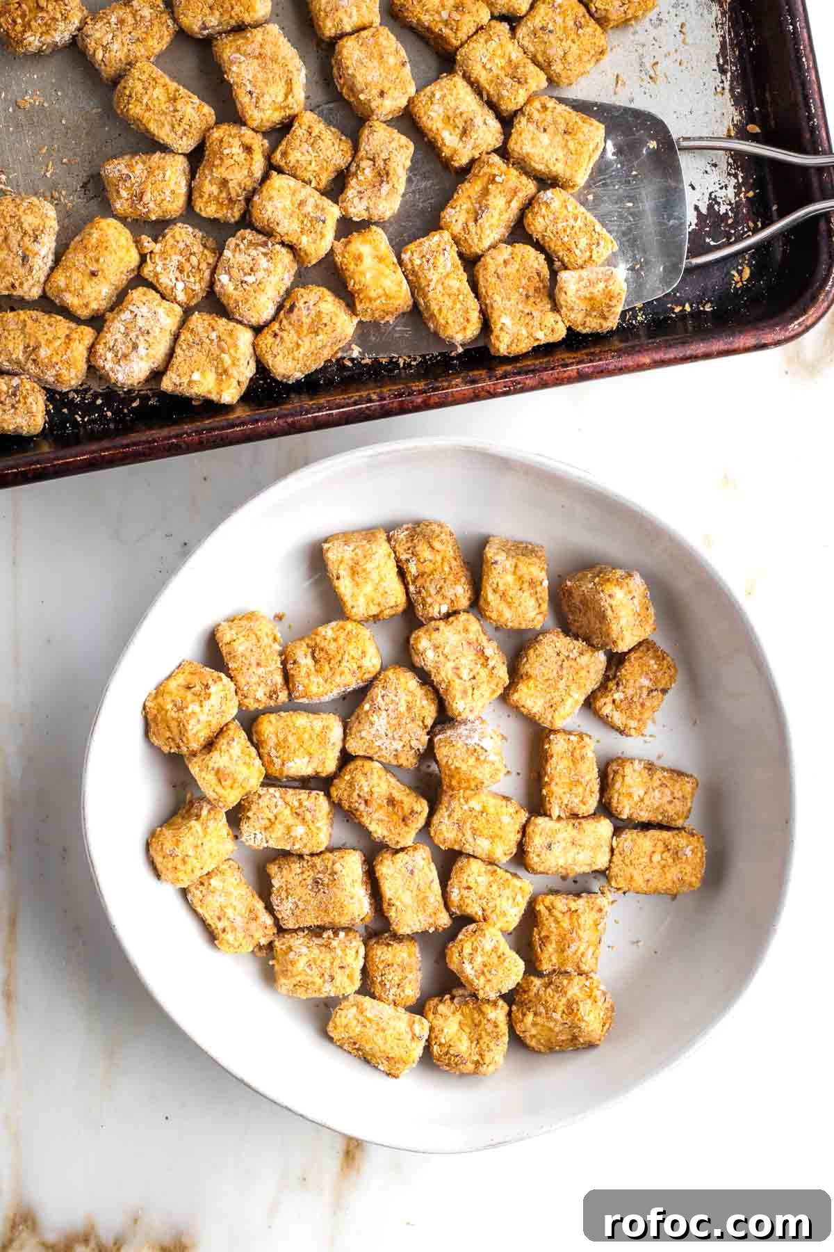 Crispy Orange Tofu — Restaurant-Style Takeout at Home 10 Spatula removing tofu from baking pan and placing crispy cubes into a serving bowl.