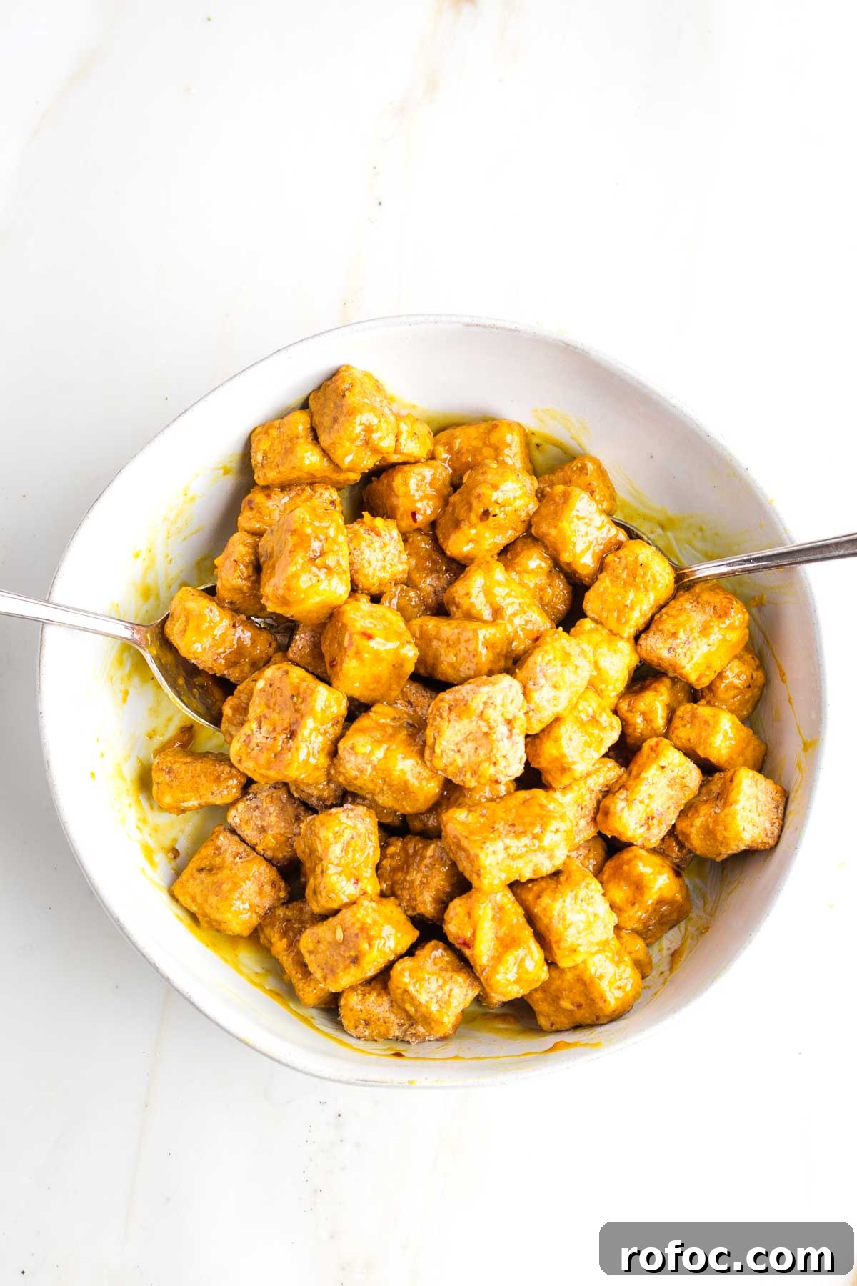 Crispy Orange Tofu — Restaurant-Style Takeout at Home 11 Cubes of crispy tofu in a bowl, smothered in orange sauce.