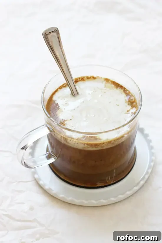 This dreamy chocolate golden milk is cozy, healthy and super simple! With warm milk, hints of vanilla, cinnamon and cocoa powder! Finished with whipped coconut cream! One mug of Chocolate Golden Milk on a white saucer with a spoon.