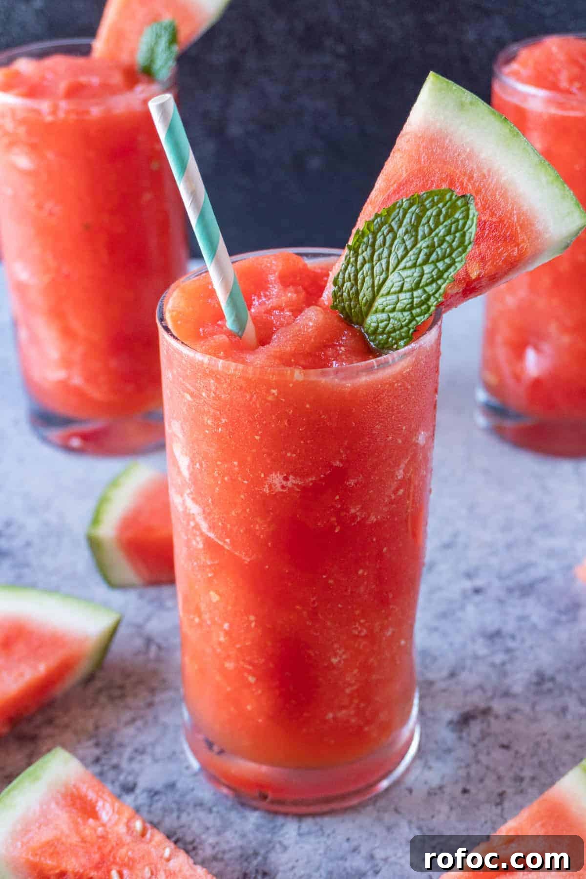 This fun watermelon drink is perfect to cool down this summer! Watermelon Slushie in cup with watermelon slice and mint leaf sticking out