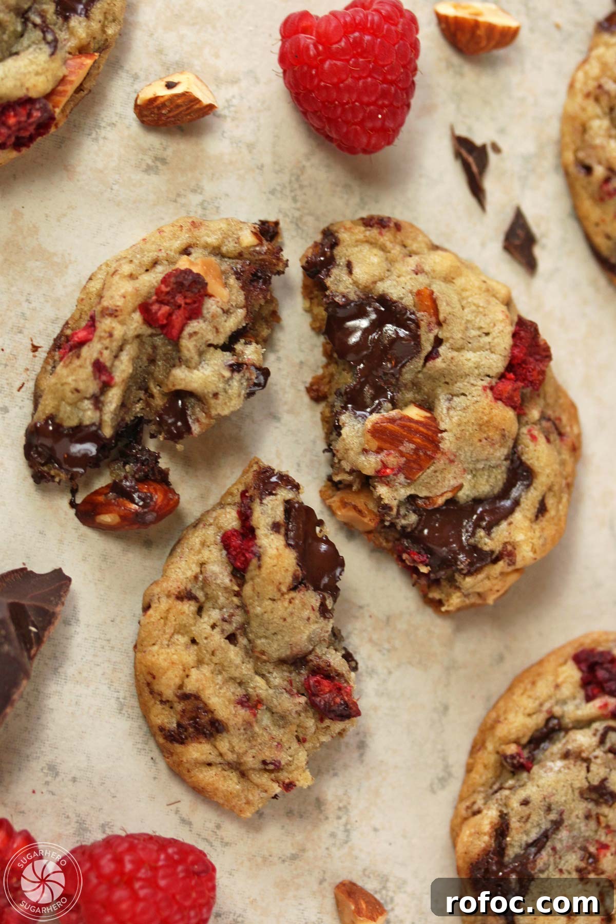 Raspberry Almond Chocolate Chunk Cookies - soft almond-flavored cookies with tangy dried raspberries and chocolate chunks. Raspberry Almond Chocolate Chunk Cookies - overhead shot of a cookie broken up on a cutting board | From SugarHero.com