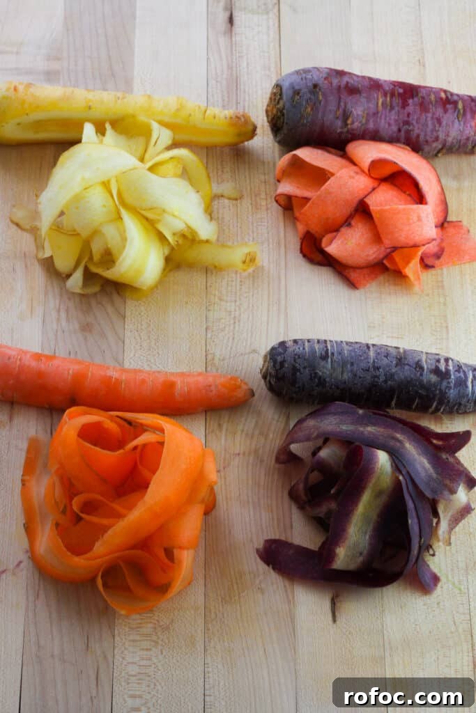 Spring Carrot and Pea Shoot Salad with Lemon Vinaigrette 4 An overhead shot on a butcher block cutting board of a yellow, purple, red and orange carrot with piles of thinly sliced carrot in front of each carrot.