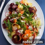 A salad on white platter on a blue table with ribbons of multicolored carrots, green pea shoots, thinly sliced radishes and sliced almonds dressed with lemon and herb vinaigrette.