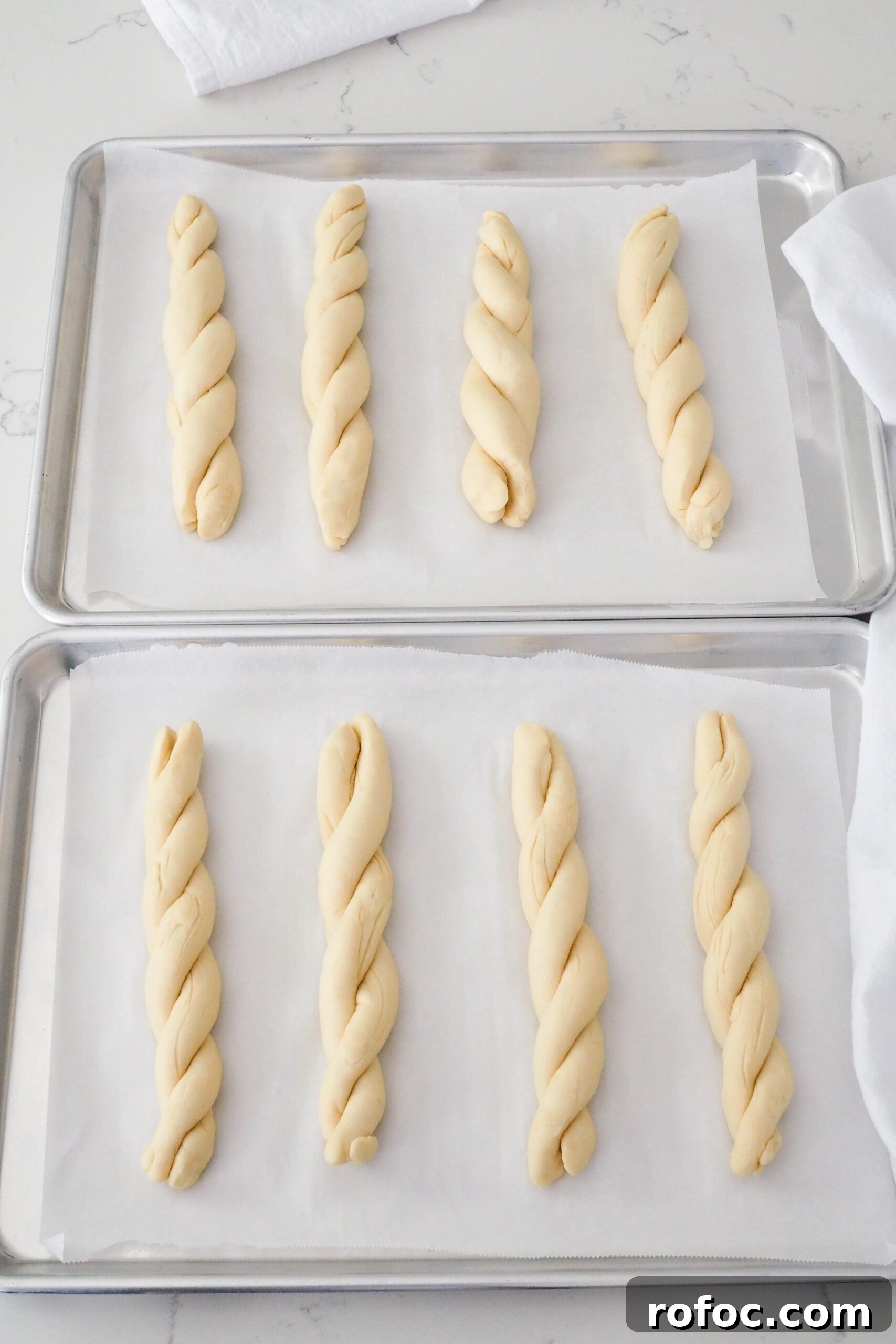 Crispy Garlic Breadsticks Recipe with Herb Butter Dip 13 Eight proofed twisted garlic breadsticks on two baking sheets.