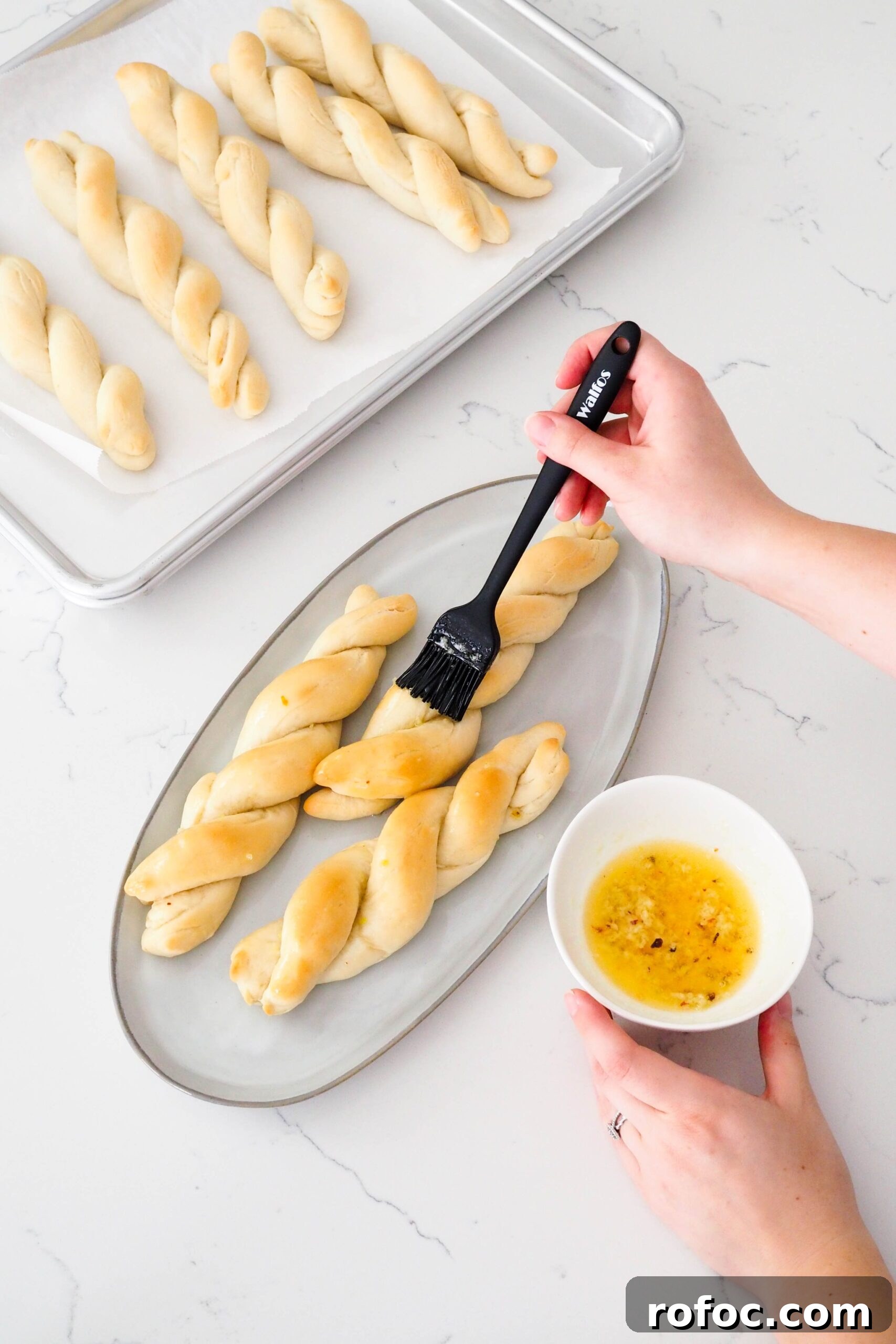 Crispy Garlic Breadsticks Recipe with Herb Butter Dip 15 A hand brushes garlic butter onto three twisted garlic breadsticks.