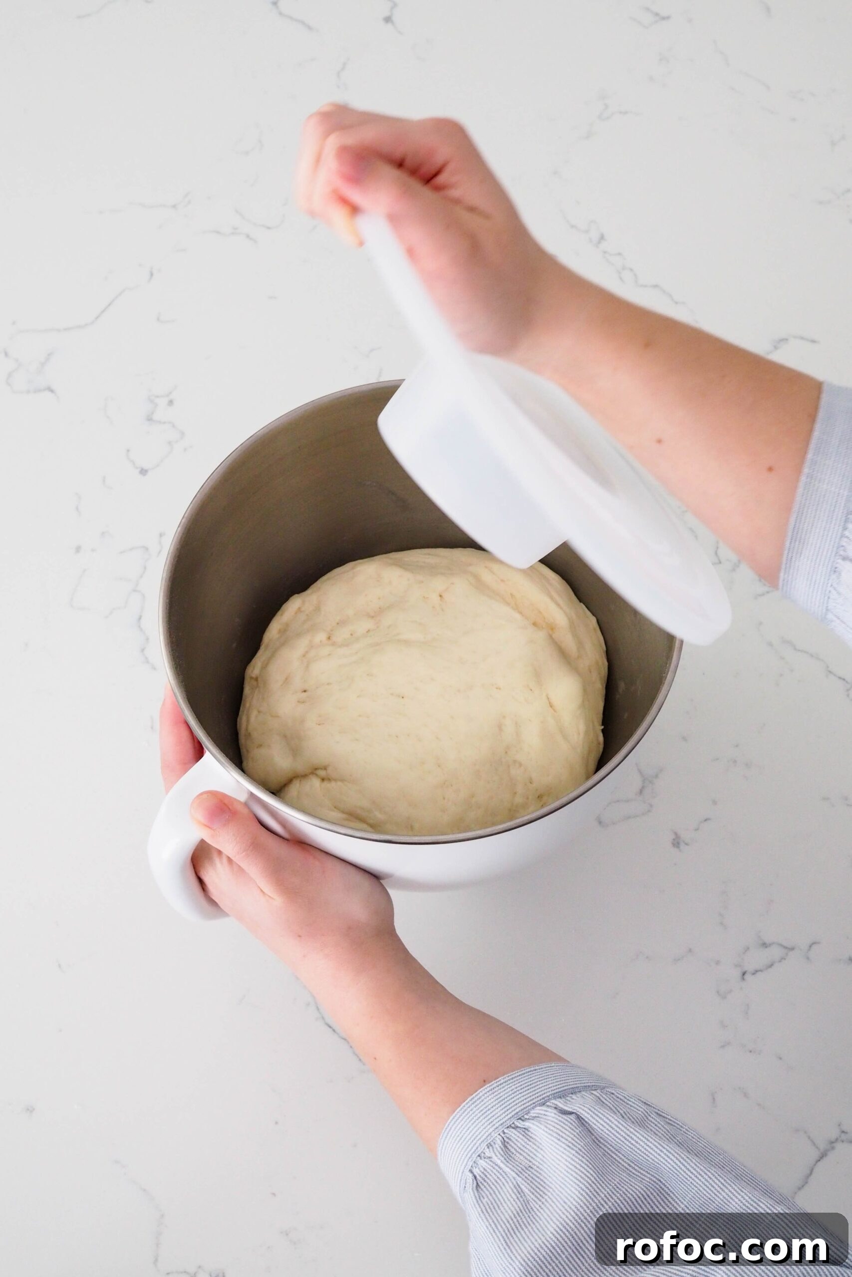 Crispy Garlic Breadsticks Recipe with Herb Butter Dip 7 A hand removes the lid off of a mixer bowl with enriched dough that has doubled in size.