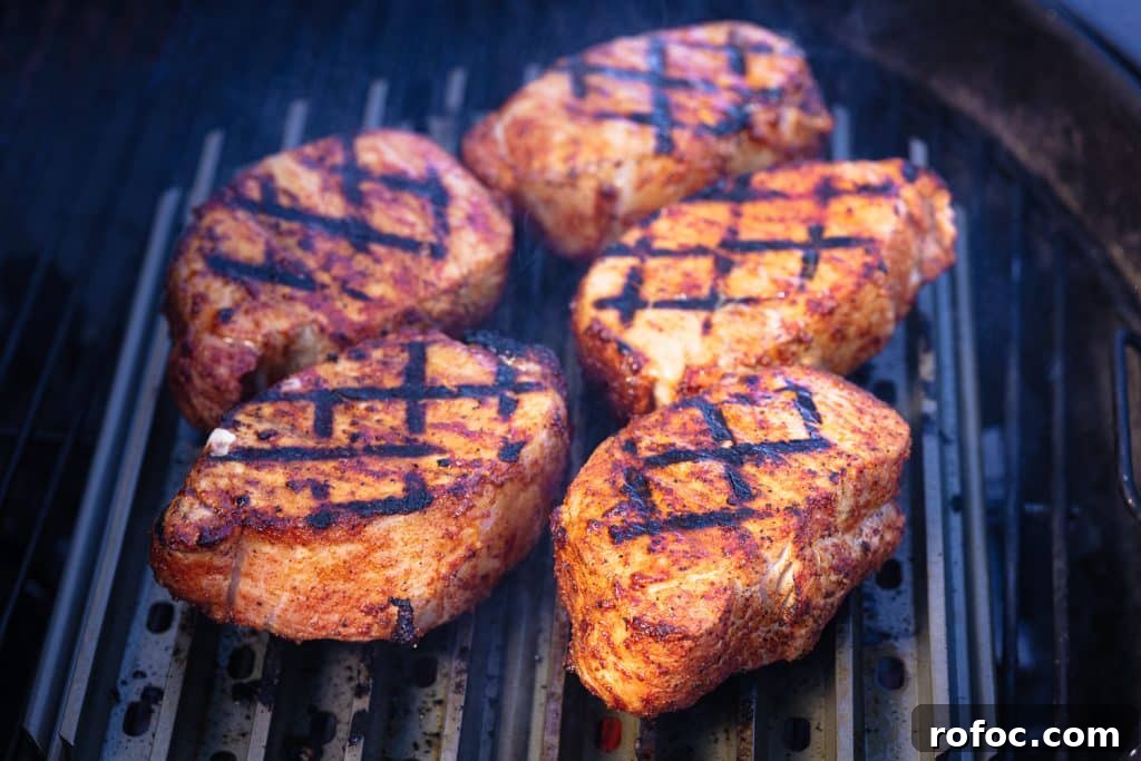 Grilled Pork Loin Chops with Caramelized Apples & Onions Recipe 5 Five pork chops cooking on grill grates.