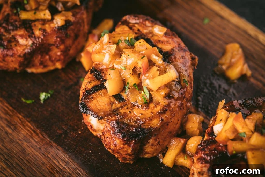 Grilled Pork Loin Chops with Caramelized Apples & Onions Recipe 7 Pork loin chop topped with grilled apples and onions on a wooden cutting board.