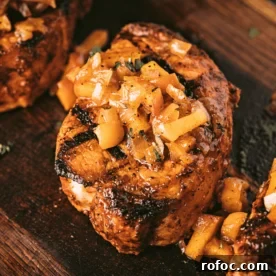 Grilled Pork Loin Chops with Caramelized Apples & Onions Recipe 8 Pork loin chop topped with grilled apples and onions on a wooden cutting board.