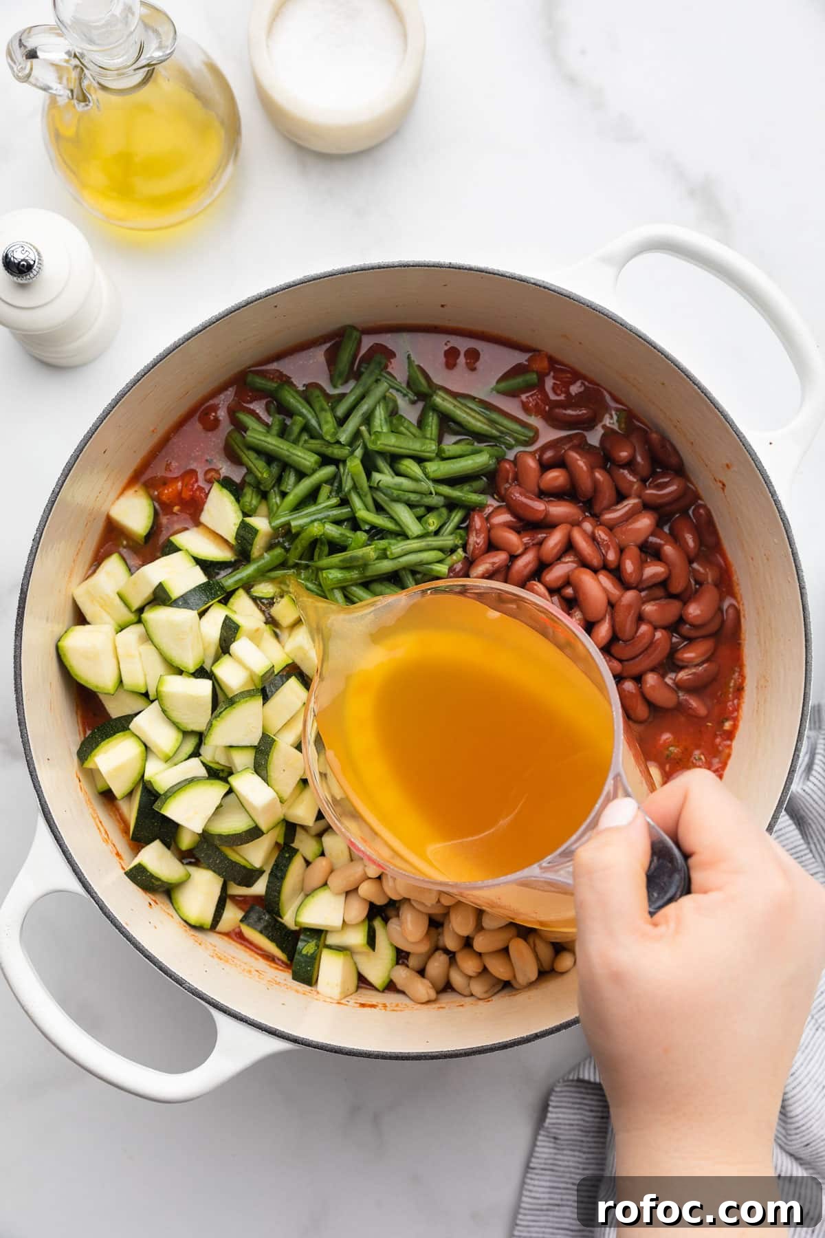 Classic Italian Minestrone Soup Recipe for Cozy Weeknight Dinners 11 pouring chicken stock into a pot of uncooked minestrone soup from a liquid measuring cup
