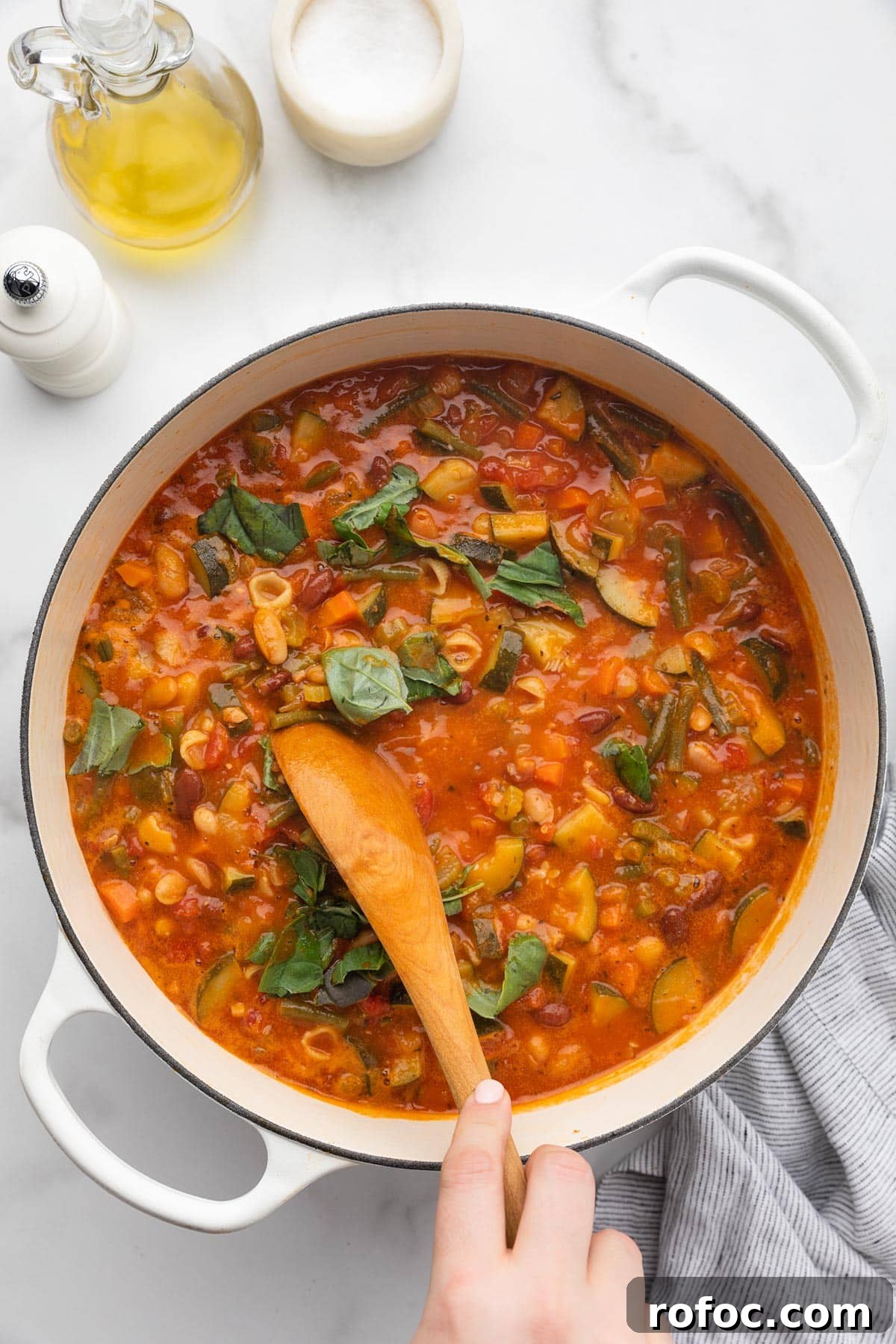 Classic Italian Minestrone Soup Recipe for Cozy Weeknight Dinners 14 stirring torn basil leaves into a pot of minestrone soup with a wooden spoon
