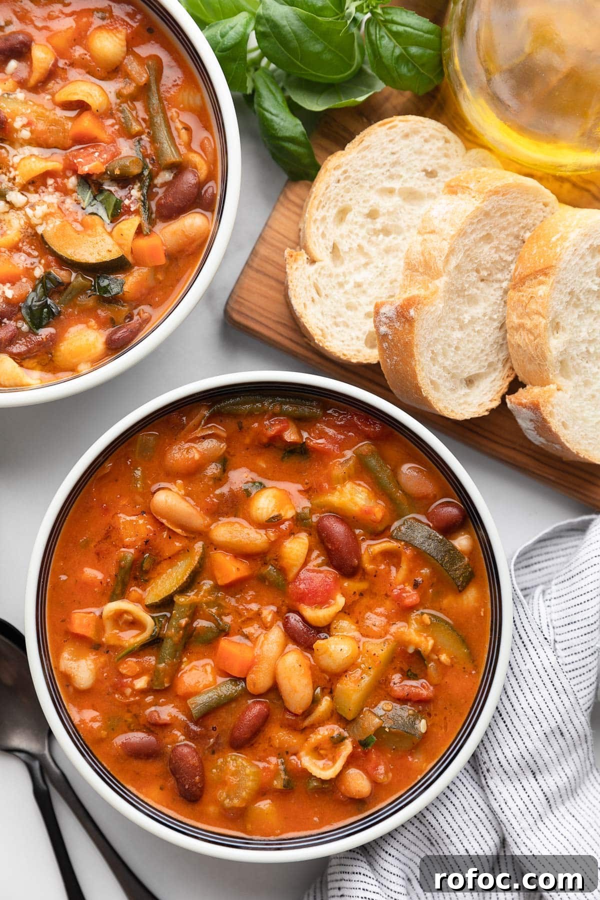 Classic Italian Minestrone Soup Recipe for Cozy Weeknight Dinners 18 overhead of two bowls of minestrone soup in a white marble board with a bread board of sliced Italian bread