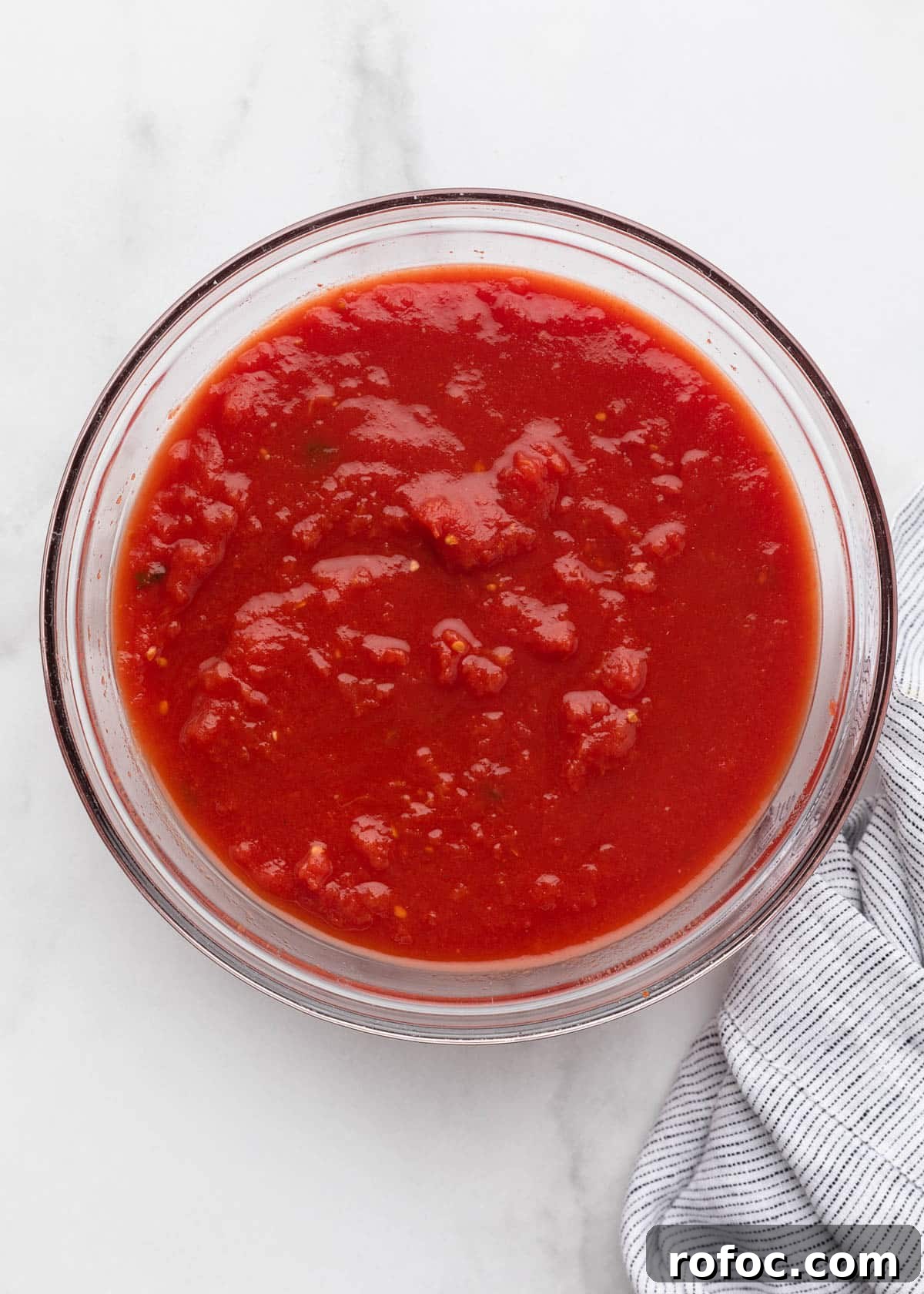 Classic Italian Minestrone Soup Recipe for Cozy Weeknight Dinners 5 hand crushed plum tomatoes in a glass bowl on a white marble surface