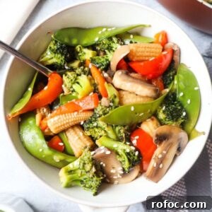 white bowl with pad pad thai which contains broccoli, snow peas, red bell peppers, mushrooms, carrot topped with sesame seeds