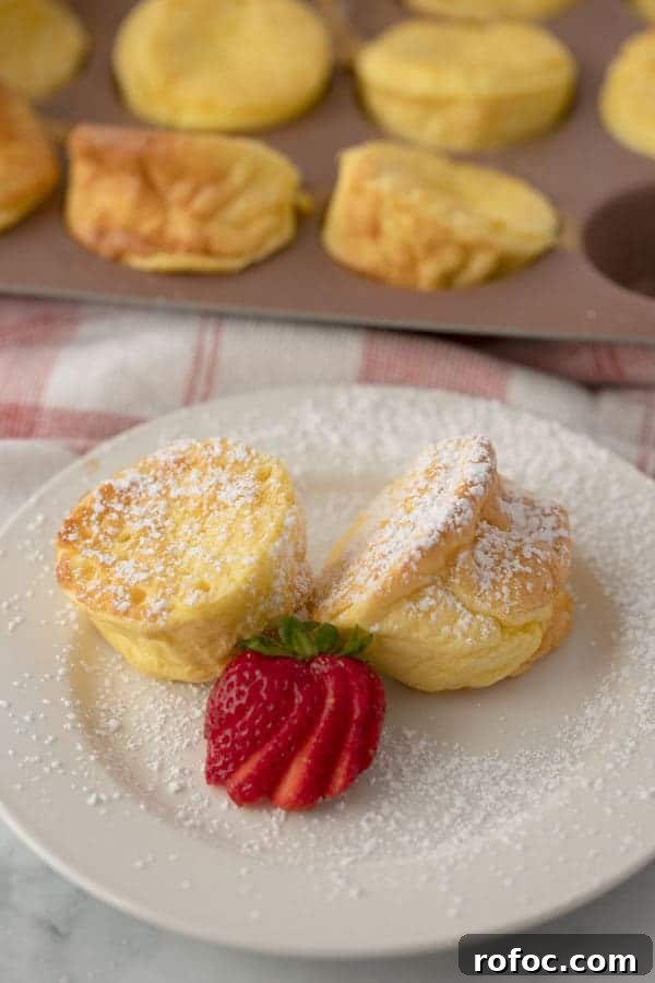 Fluffy German Pancake (Dutch Baby) Recipe + Video Guide 4 Individual sized German pancakes on a small plate topped with powdered sugar and a fresh strawberry.