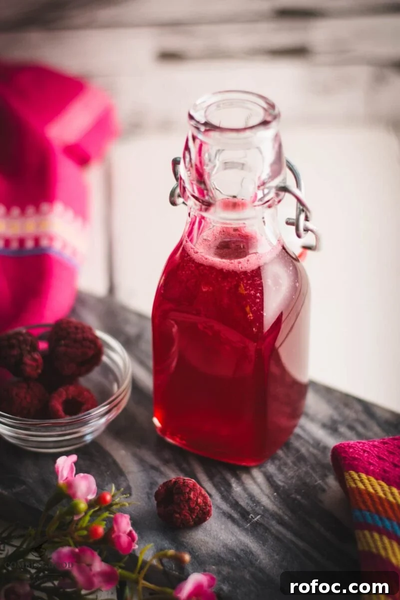 No-Cook Homemade Raspberry Syrup Recipe for Fresh, Intense Flavor 2 Preserving bottle, filled with delicious uncooked raspberry syrup placed on a marbled plate.