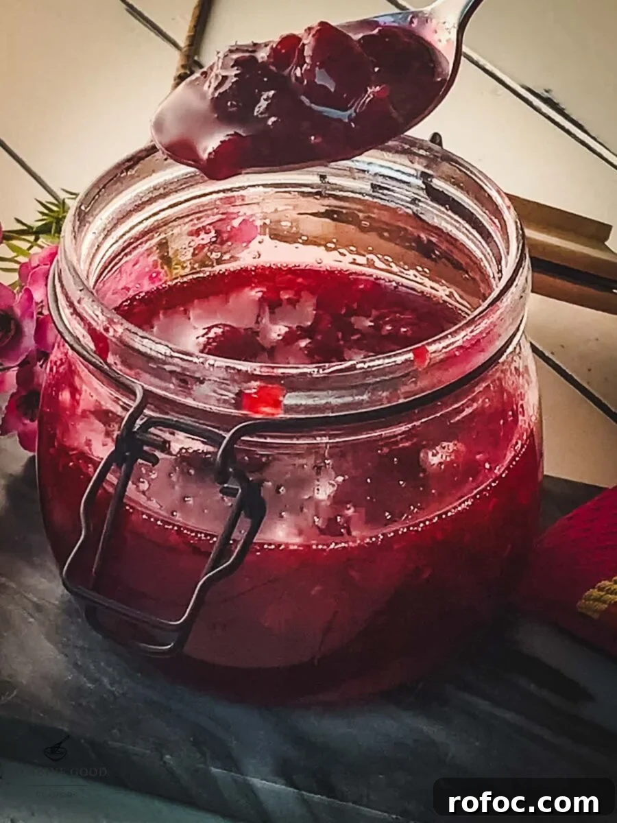 No-Cook Homemade Raspberry Syrup Recipe for Fresh, Intense Flavor 6 Spoon with raspberry sauce hovering over a preserving jar filled with raspberry sauce.