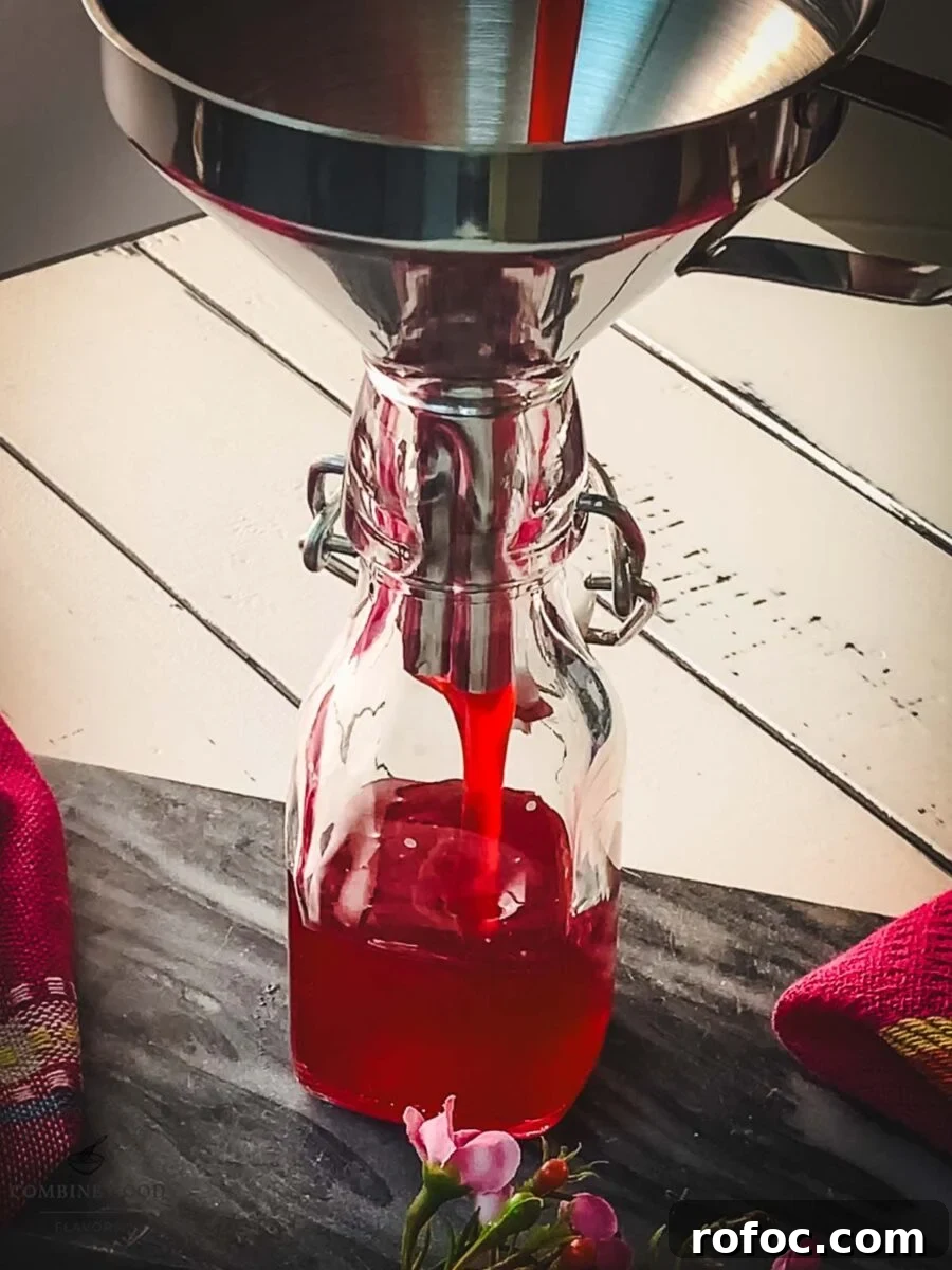 No-Cook Homemade Raspberry Syrup Recipe for Fresh, Intense Flavor 8 Pouring the finished raspberry syrup into a preserving bottle using a funnel.