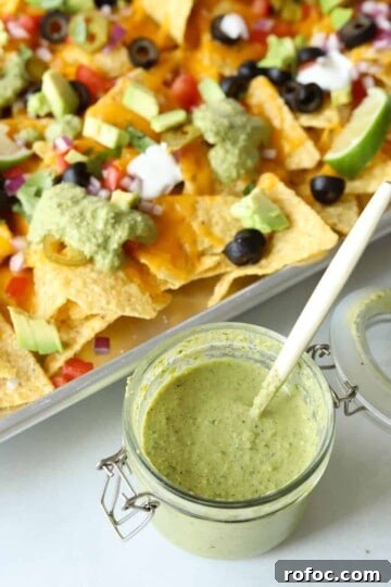 jar of creamy poblano sauce with spoon in it with nachos in background