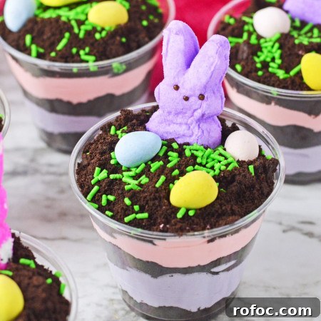 Easter Dirt Cup Treats: Chocolate Pudding Parfaits with Oreo Soil 7 Easter dirt cups with layered instant pudding in colors, topped with peeps and mini eggs.