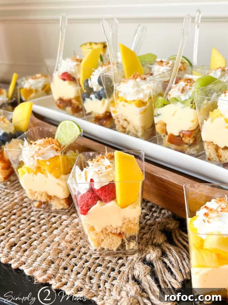9 Tropical Cocktail Appetizers for Your Next Party 12 Mini plastic cups of keto tropical trifle parfaits with a variety of diced fruit on a white platter.
