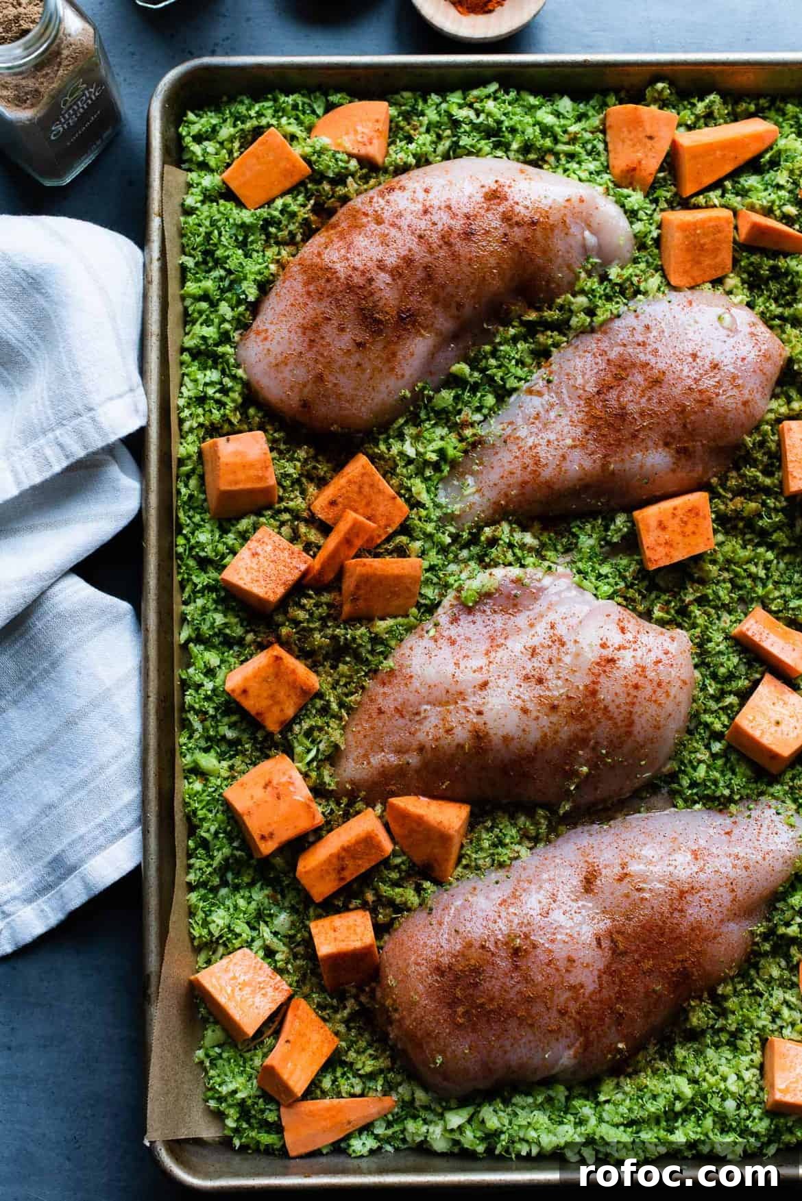 Sheet-Pan Moroccan Chicken with Broccoli Rice & Roasted Sweet Potatoes 5 Chopped sweet potatoes, broccoli rice, and seasoned chicken breasts on a baking tray ready to bake.