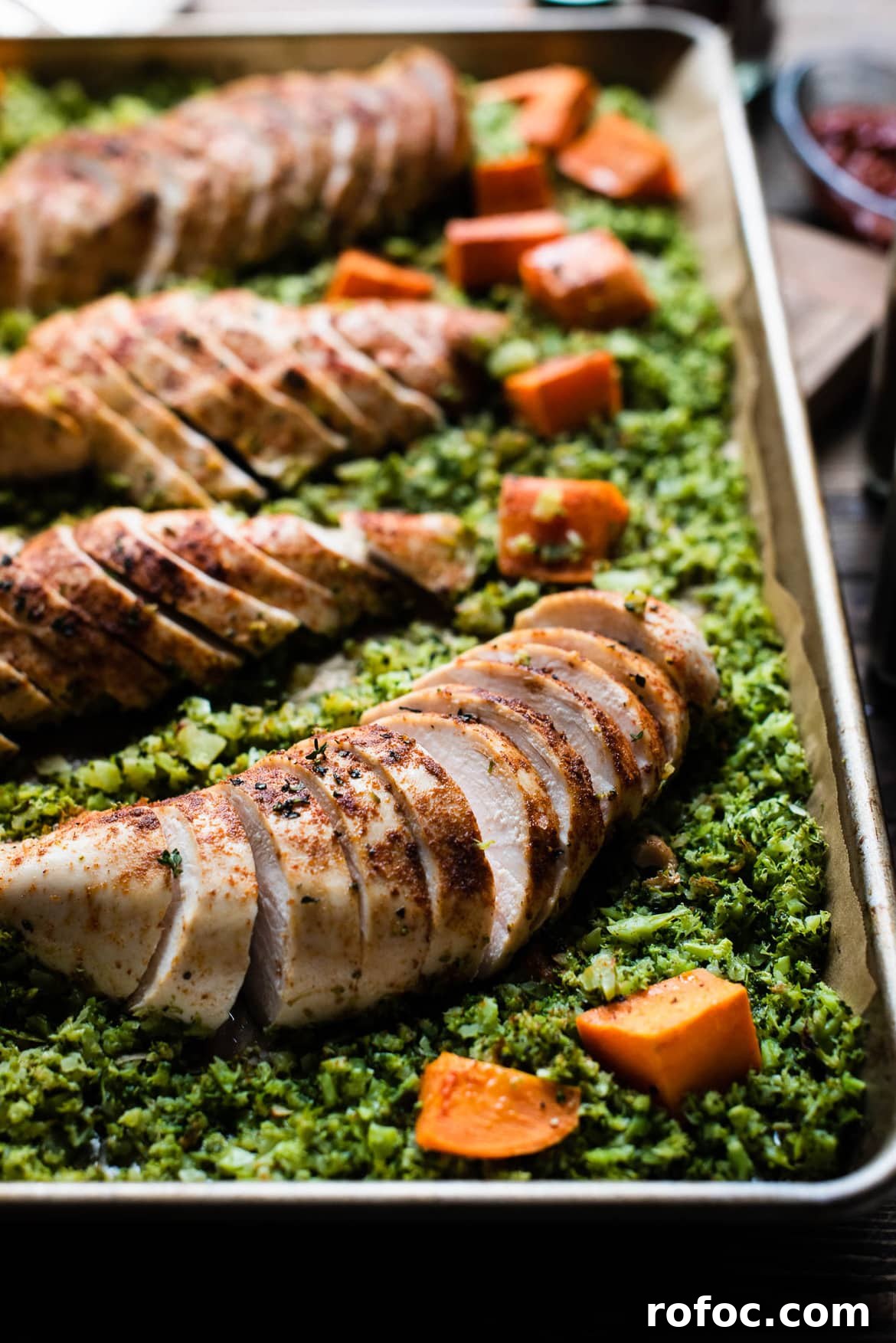 Sheet-Pan Moroccan Chicken with Broccoli Rice & Roasted Sweet Potatoes 9 A sliced seasoned chicken breast surrounded by broccoli rice and sweet potato chunks.