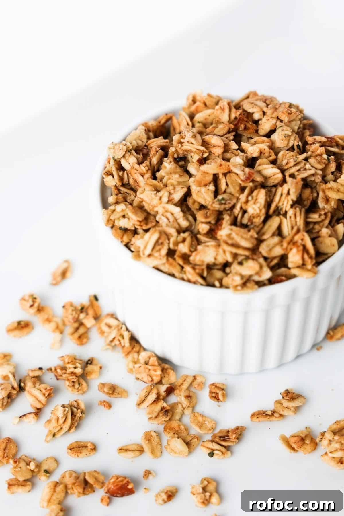 Low-Sugar Homemade Granola Recipe for Crunchy Breakfast 2 Granola in a white ramekin with pieces of granola scattered around the ramekin.