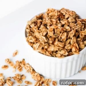 Low-Sugar Homemade Granola Recipe for Crunchy Breakfast 9 Granola in a white ramekin with pieces of granola scattered around the base of the ramekin.